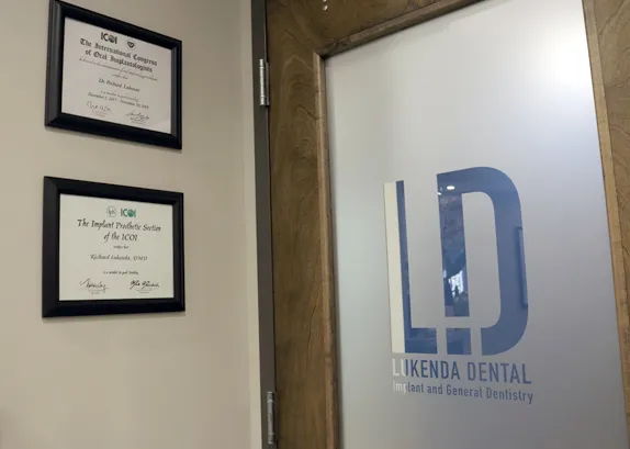 Two framed ICOI certificates on the wall beside the frosted glass door — the International Congress of Oral Implantologists and its Implant Prosthetic Section, both awarded to Richard Lukenda