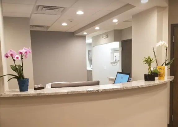 Reception desk at Lukenda Dental — a curved granite counter with orchids and a screen